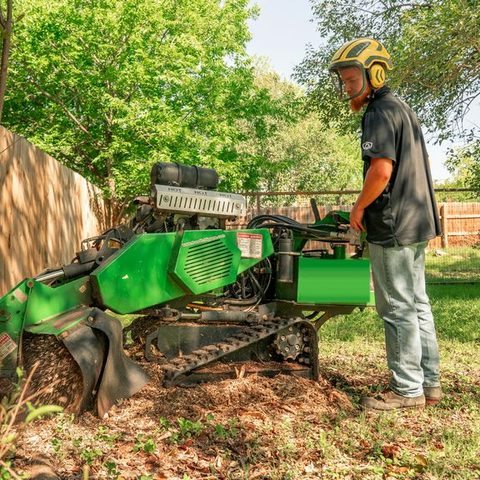 Operator running a stump grinder beside a wooden fence